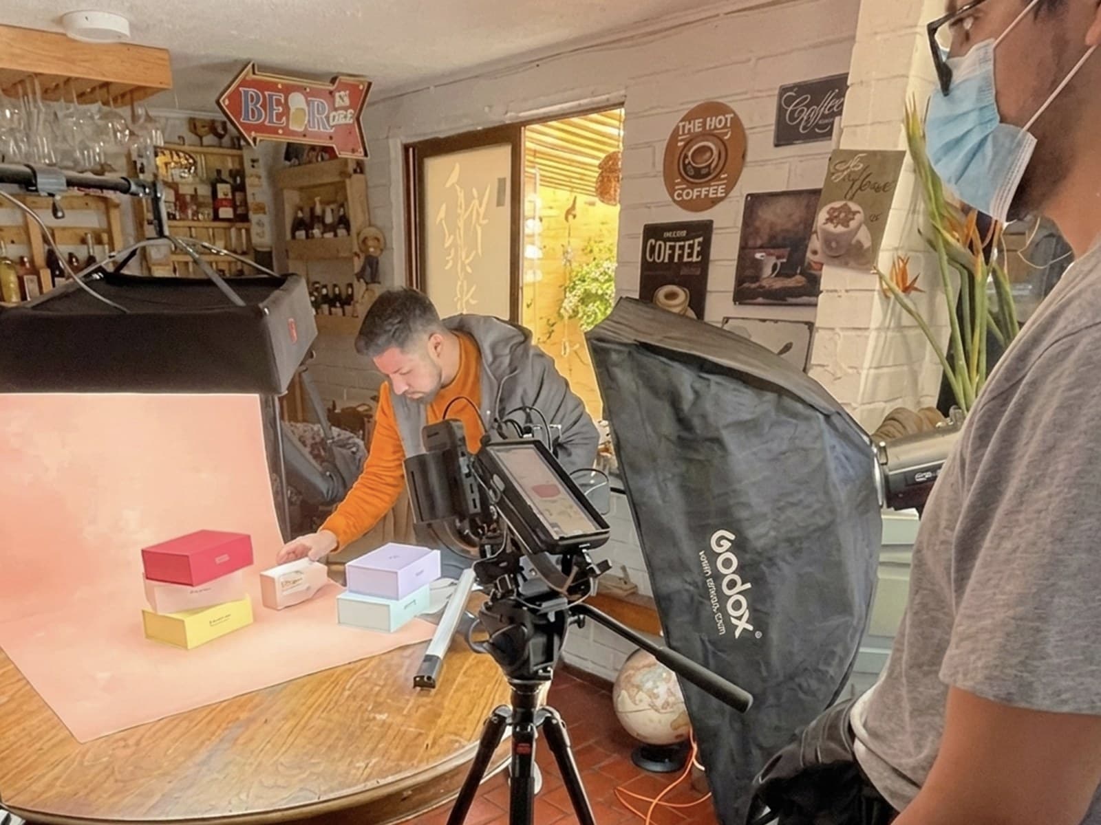 Detrás de cámara de una jornada de TMI para Beppy: una persona ordena cajas de la marca sobre un fondo rosado, frente a una cámara con monitor y una luz con softbox.